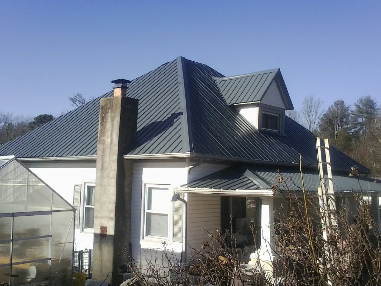 Dark blue standing seam metal roof on a white farmhouse with dormer — Slate & Tile Roof Repair by Roofing Brothers in Center City