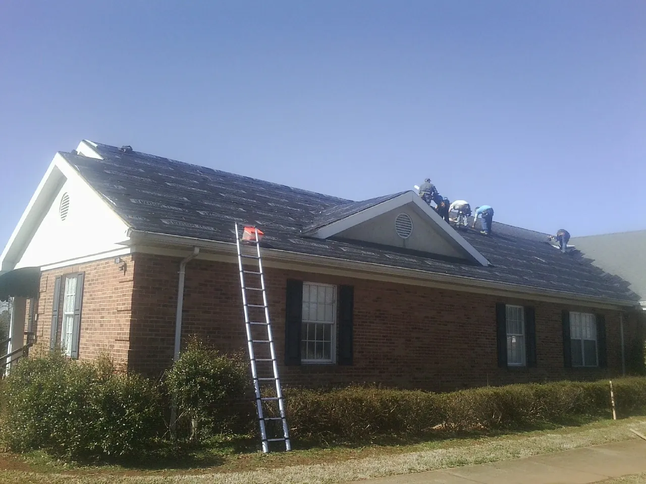 Crew tearing shingles off a brick ranch roof with a ladder set — Emergency Roof Repair work by our crew in Center City