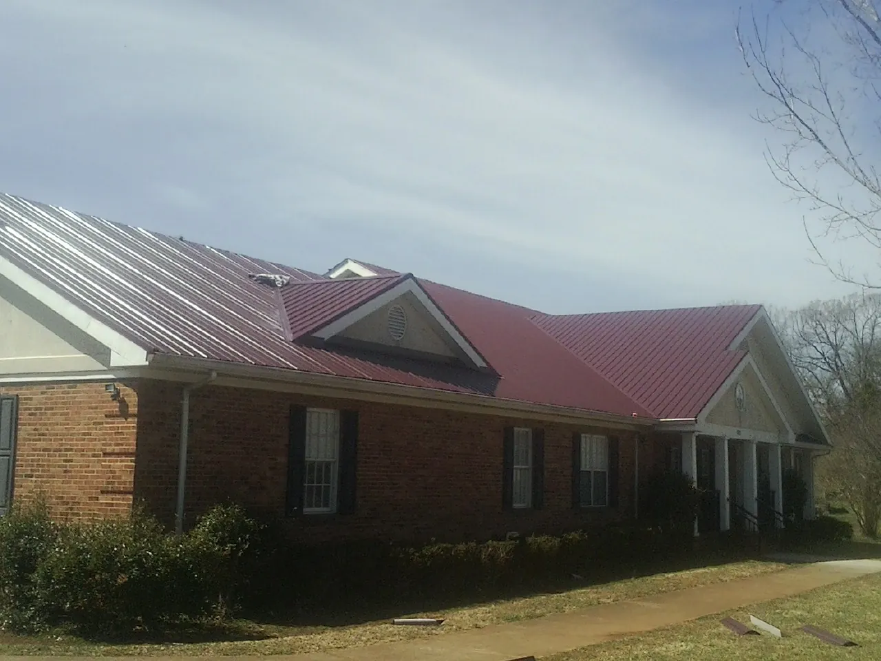 Red metal roof with gabled entries on a long brick building, from a Hail Damage Roof Repair job in Center City