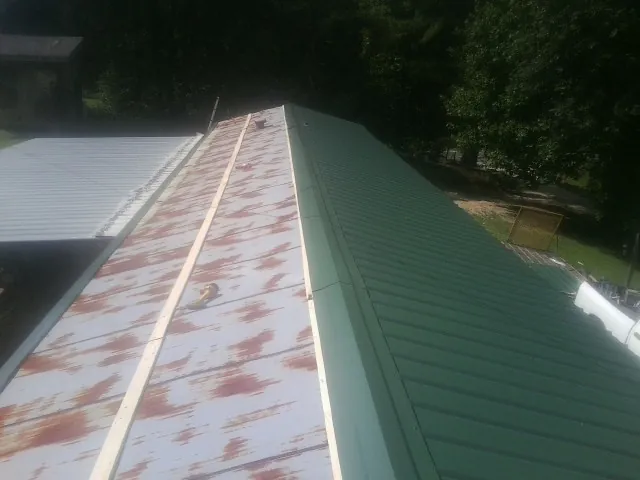 Old rusted panels beside newly installed green metal roofing — Wind Damage Roof Repair by Roofing Brothers in Center City