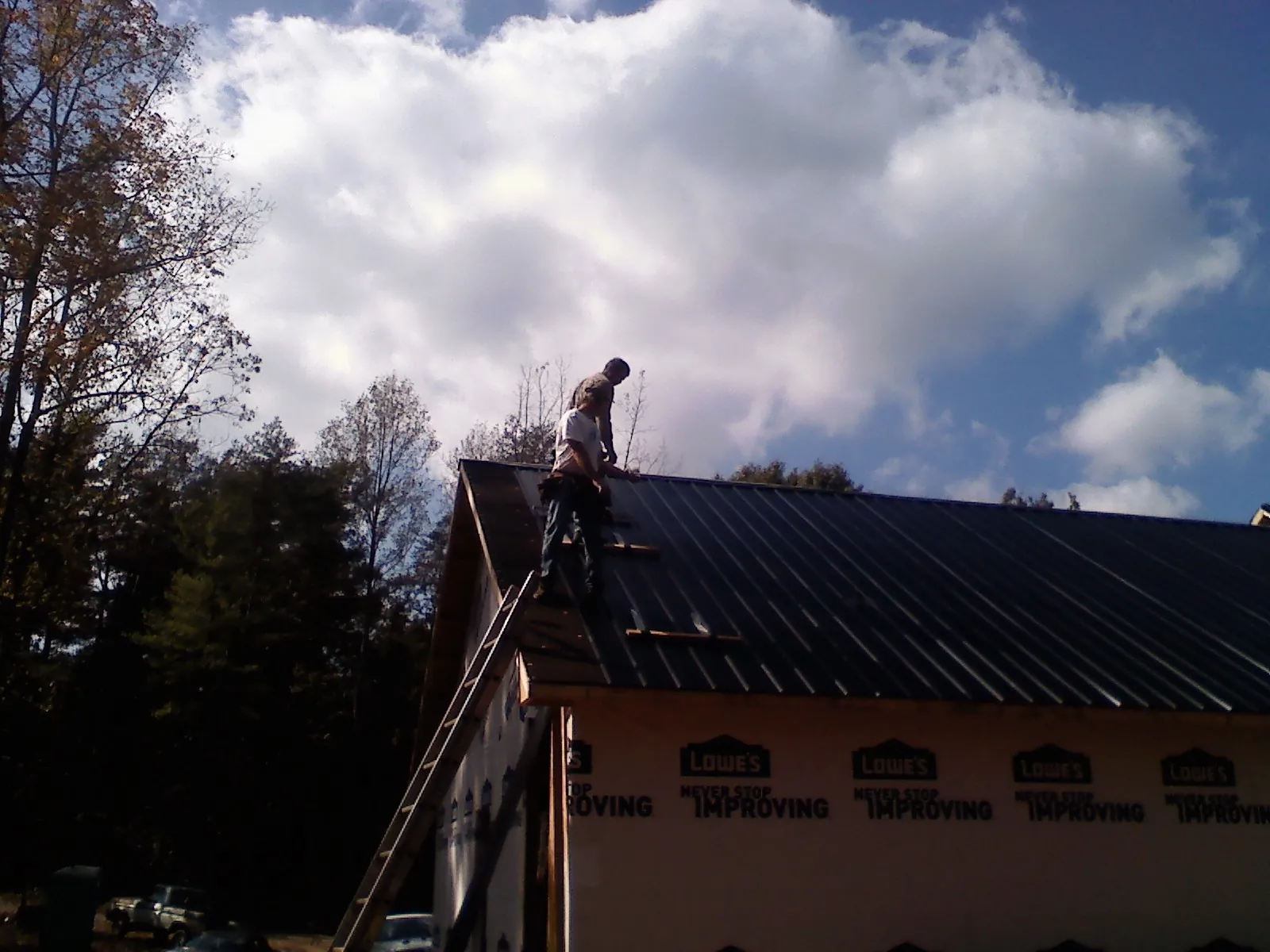Roofer fastening dark metal panels high against a cloudy sky, from a Roof Inspection job in Center City
