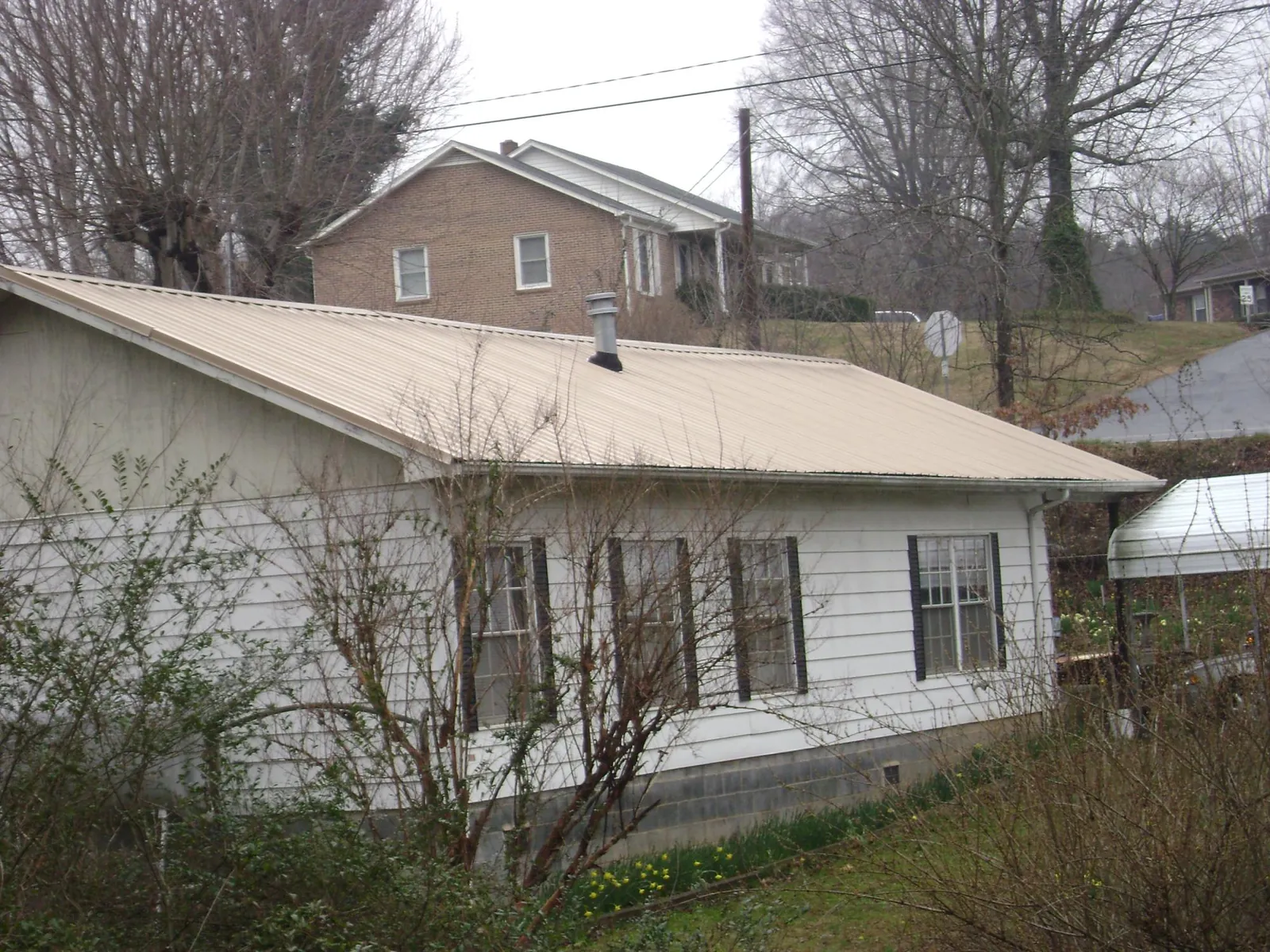 Tan metal roof on a white sided house set into a hillside — Commercial Roofing by Roofing Brothers in Center City